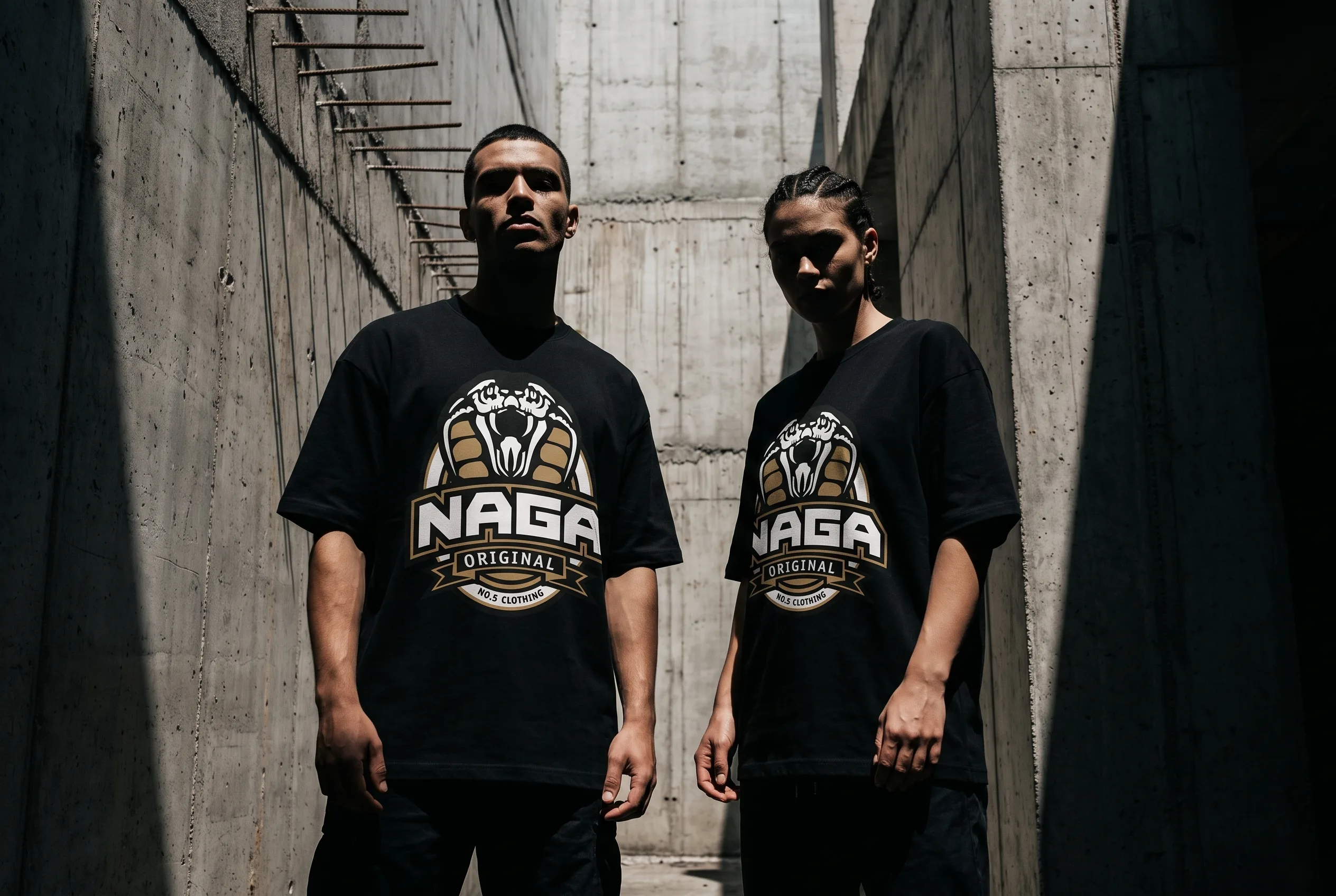 Two models in black Naga Original graphic tees against raw concrete walls